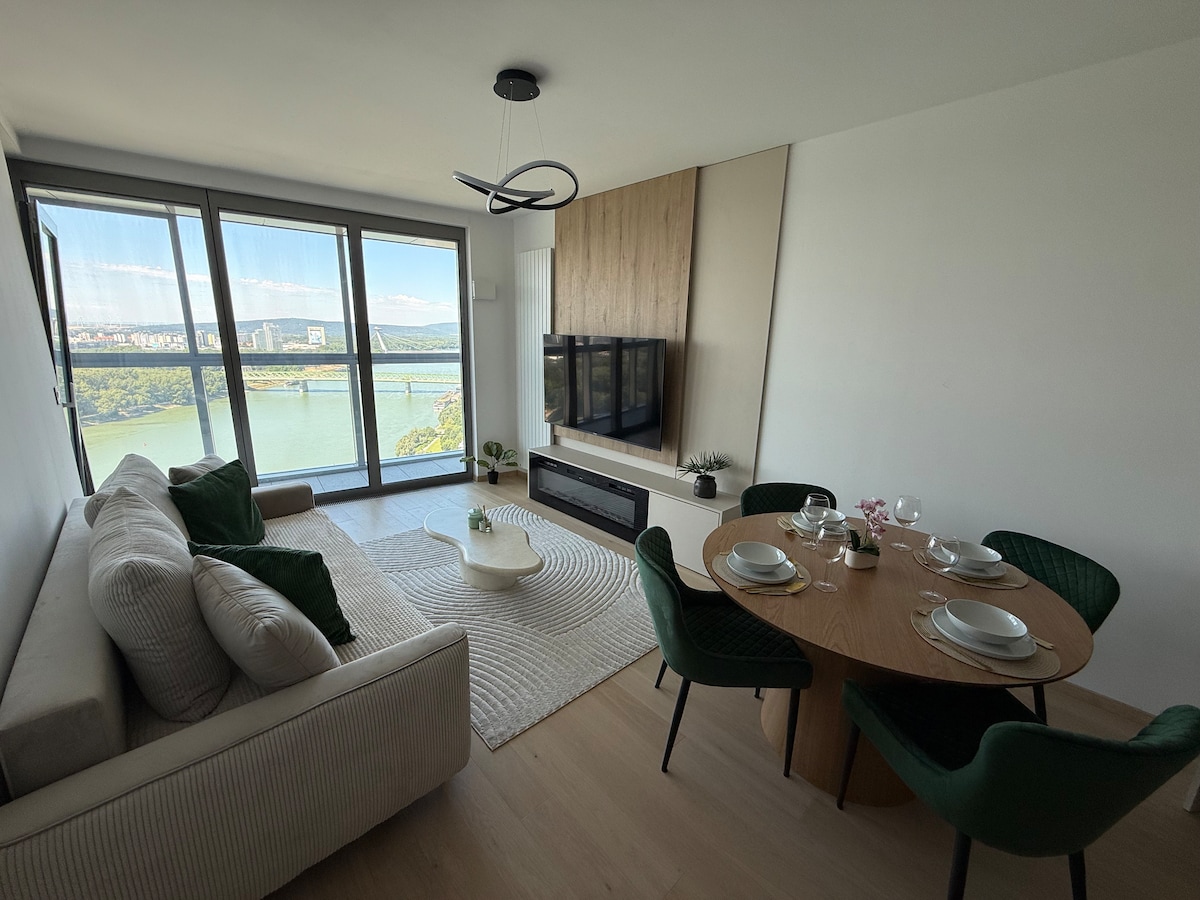 Denná zóna bytu Eurovea Tower so sedačkou, jedálenským stolom a presklenou stenou s výhľadom na Dunaj